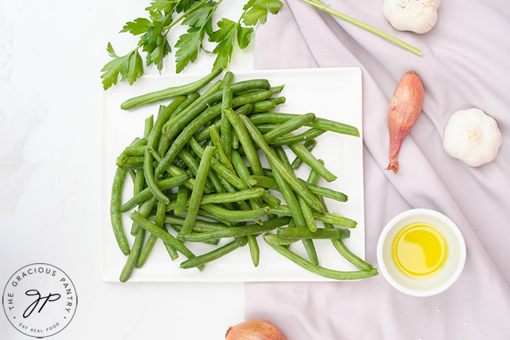 String Beans, a shallot, oil and garlic all gathered on a white surface.