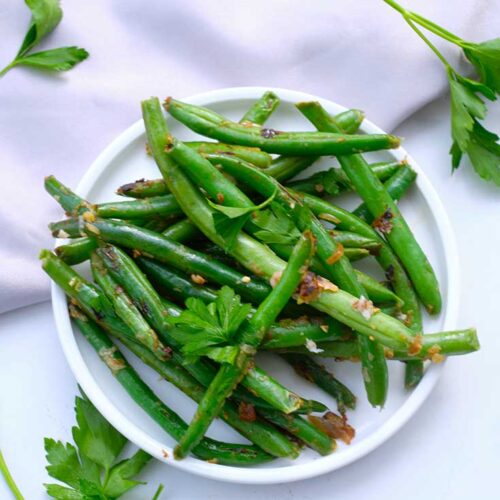 An overhead view looking down on a white plate filled with Garlicky Green Beans and garnished with fresh parsley.