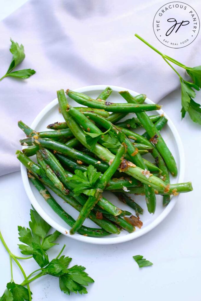 An overhead view looking down on a white plate filled with Garlicky Green Beans and garnished with fresh parsley.