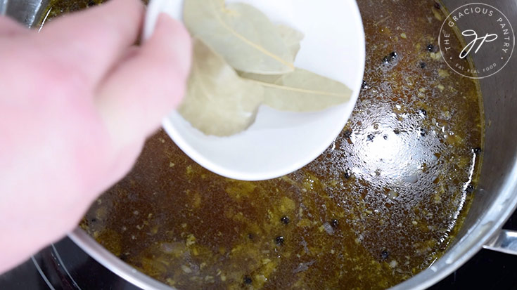 Putting bay leaves into broth in a soup pot.