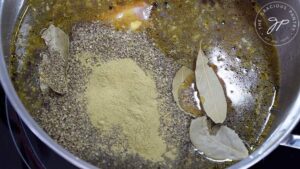 Bay leaves, ground black pepper and ground rosemary floating in a pot of broth, veggies and chicken.