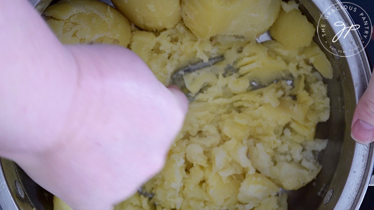 Mashing potatoes in a pot with a fork to make German potato dumpling soup.