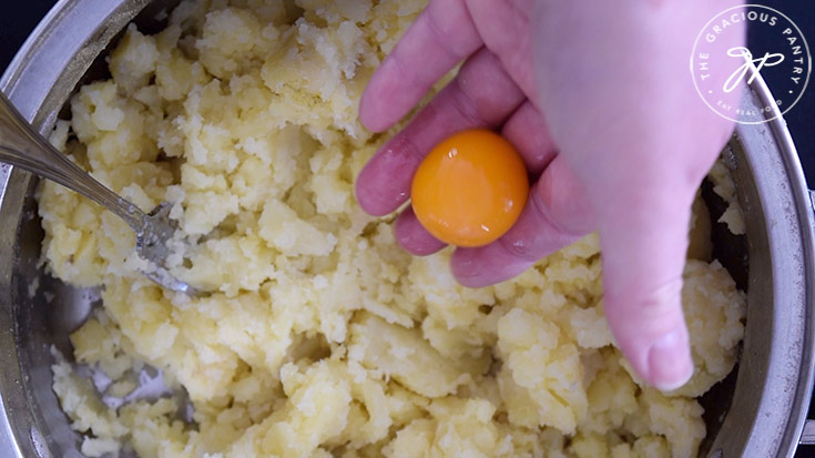 Adding egg yolks to smashed potatoes in a pot.