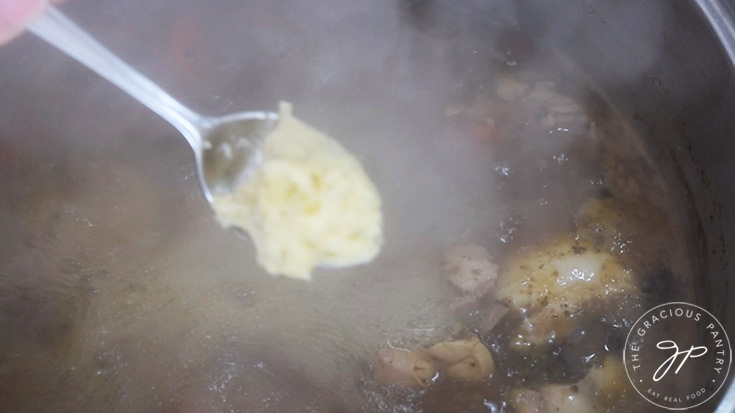 A spoon picks up a small amount of the smashed potatoes to form a dumpling for this German potato dumpling soup.