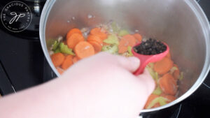 Adding peppercorns to sautéd veggies in a soup pot.