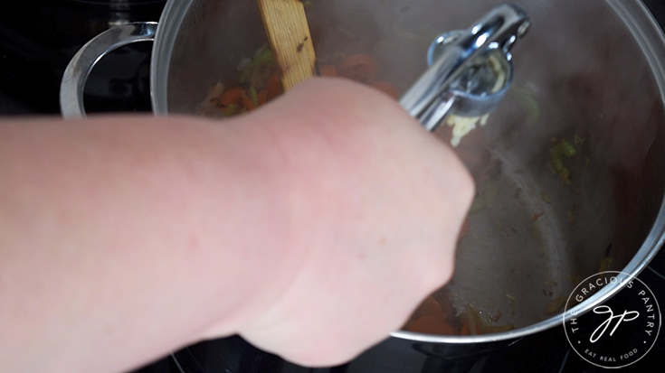 Pressing fresh garlic into a soup pot through a garlic press.