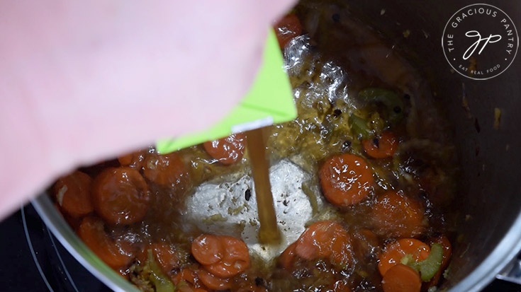 Adding broth for the German potato dumpling soup to a large soup pot.