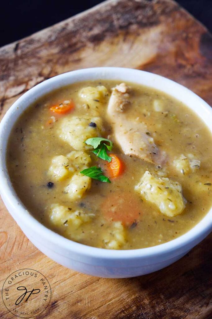 A side view of a white bowl filled with German Potato Dumpling Soup, sitting on a wooden surface.