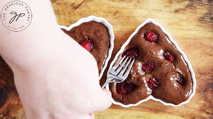 Pressing fresh raspberries into raw Healthy Chocolate Raspberry Cake batter in two heart-shaped ramekins.