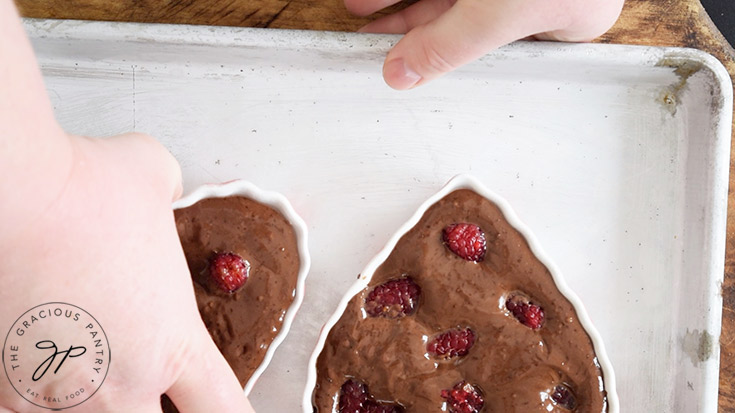 Placing two heart-shaped ramekins filled with Healthy Chocolate Raspberry Cake batter on a baking pan.