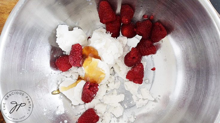 Fresh raspberries and honey added to coconut cream in a mixing bowl.