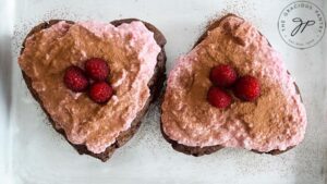 Two Healthy Chocolate Raspberry Cakes garnished with fresh raspberries, frosting and cocoa powder.