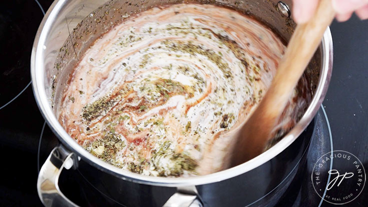 Stirring together all the Healthy Tomato Soup Recipe ingredients in a pot on a stovetop.