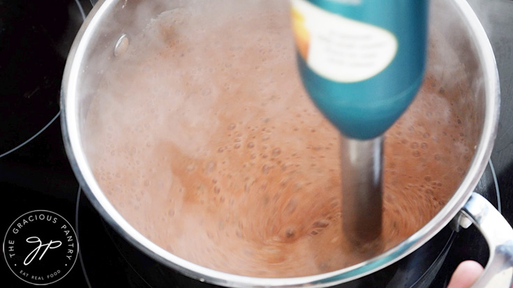 Blending the Healthy Tomato Soup with a stick blender in a pot on a stovetop.