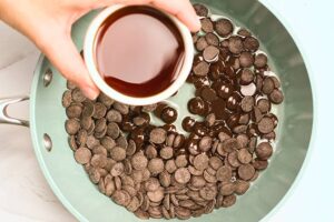 Pouring maple syrup into melting chocolate chips in a skillet.