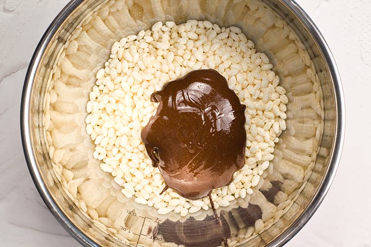 Homemade Crunch Bars batter added to a bowl filled with brown puffed rice cereal.