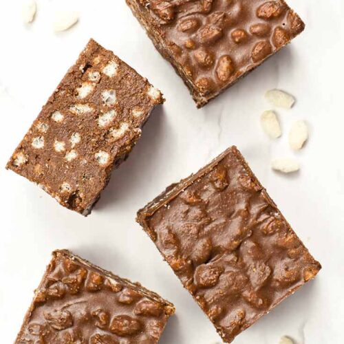 An overhead view looking down on four Homemade Crunch Bars and some puffed brown rice on a white surface.