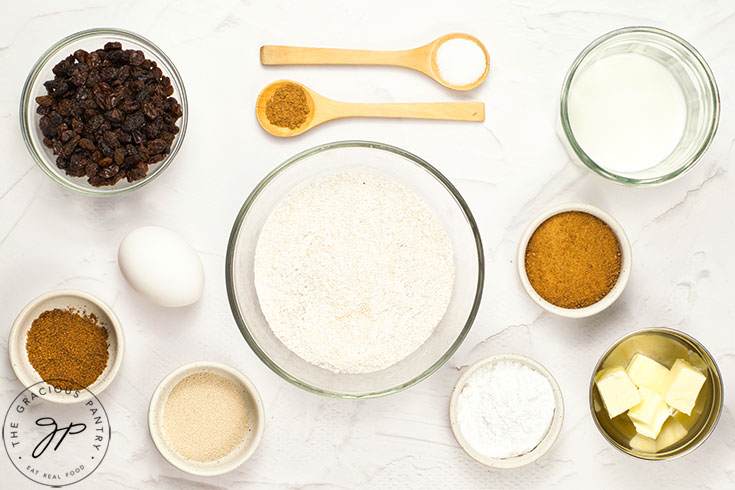 Hot cross bun recipe ingredients on a white surface, in individual bowls.