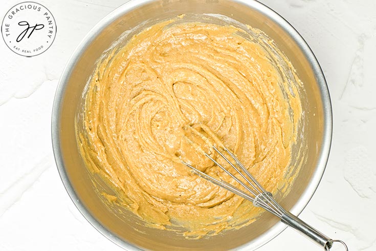 Raw, hot cross bun batter sitting in a mixing bowl with a whisk.