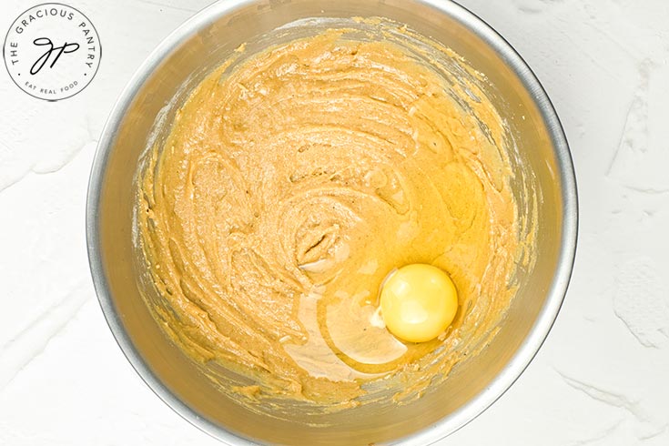 Hot cross bun batter with an egg sitting on top of the raw batter in a mixing bowl.