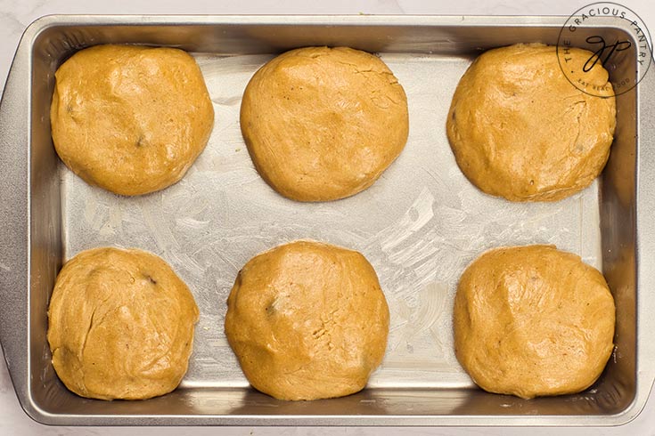 6 uncooked hot cross buns sitting in a parchment-lined baking pan.