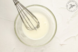 A mixing bowl sits with icing and a whisk inside it.