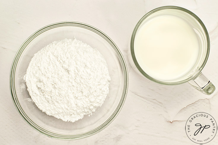 Milk and powdered sweetener sit in idividual bowls on a white surface.