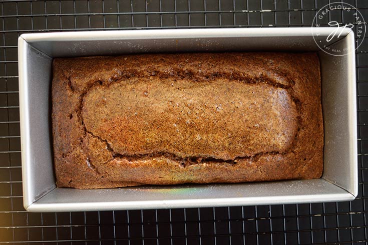 A just-baked Pecan Butter Bread loaf cooling on a wire rack in a loaf pan.