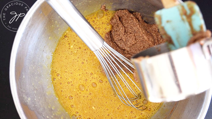 Adding pecan butter to an egg mixture in a mixing bowl.