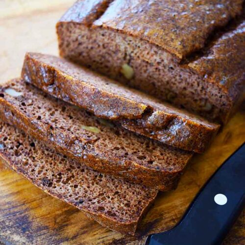 A loaf of Pecan Butter Bread sitting on a cutting board with three slices cut from the loaf.