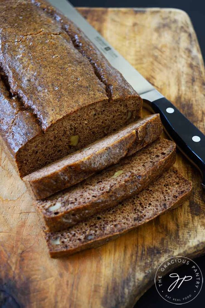 A loaf of partially sliced pecan butter bread sits on a cutting board. A bread knife lays next to the loaf.