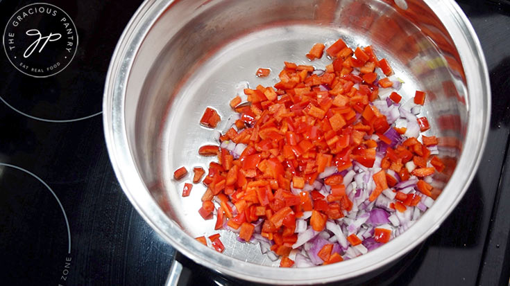 Chopped red bell pepper and red onion sautéing in a large pot in oil.