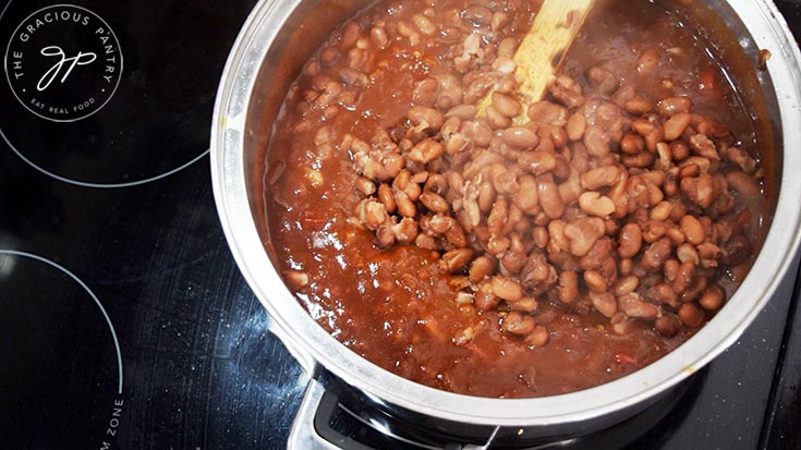 Adding cooked pinto beans to a pot of Ranch Style Beans sauce.