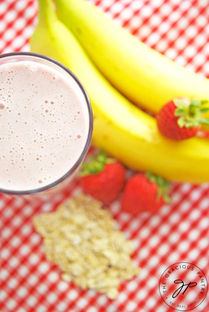 An overhead shot looking down on a glass of Strawberry Oatmeal Smoothie next to some bananas, strawberries and oats.
