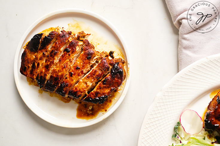 A cooked Balsamic Pork Chop on a white plate, cut and ready to enjoy.