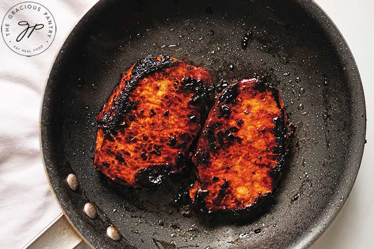 Two Balsamic Pork Chops cooking in a skillet.