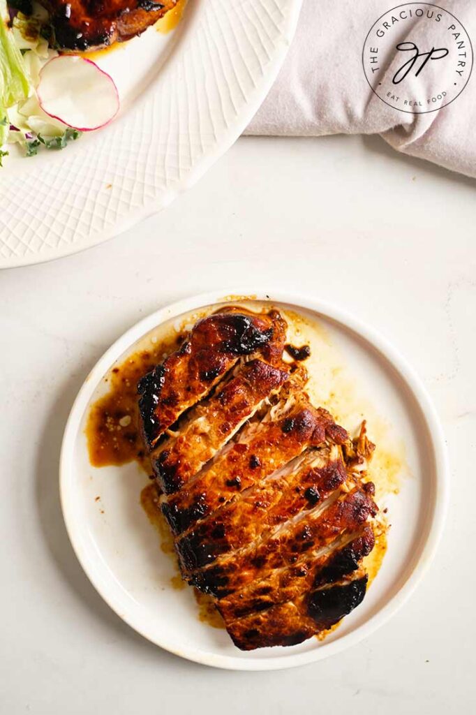 An overhead view looking down on a single, cooked, balsamic pork chop, sliced and served on a white plate.