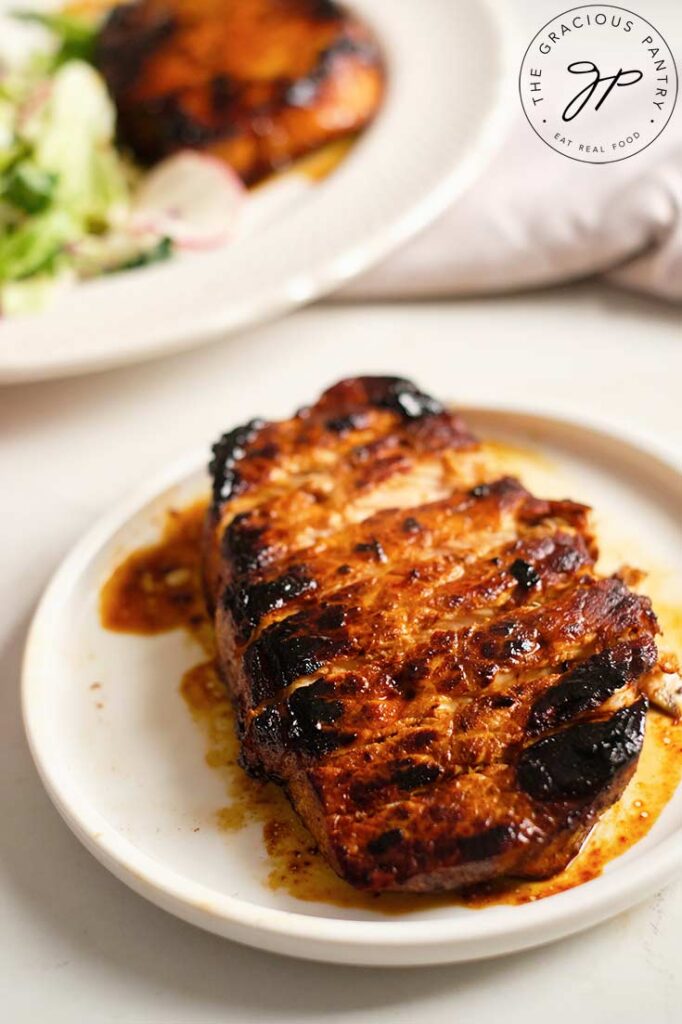 A front view of a single, cooked, balsamic pork chop, sliced and served on a white plate.