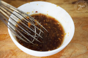 A whisk resting in a small white bowl which holds some Chinese Garlic Sauce.