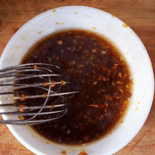 An overhead view of a whisk resting in a small white bowl of Chinese Garlic Sauce.