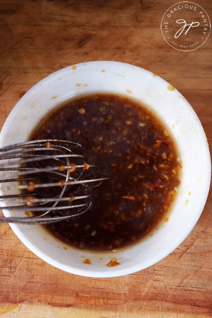 An overhead view of a whisk resting in a small white bowl of Chinese Garlic Sauce.