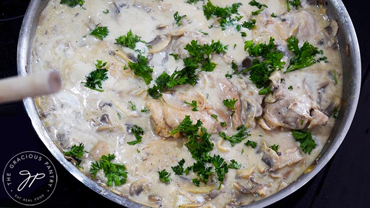 Garnishing a skillet full of Creamy Garlic Mushroom Chicken with fresh parsley.