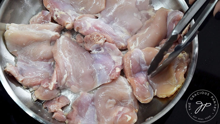 Adding chicken thighs to a hot pan with oil.