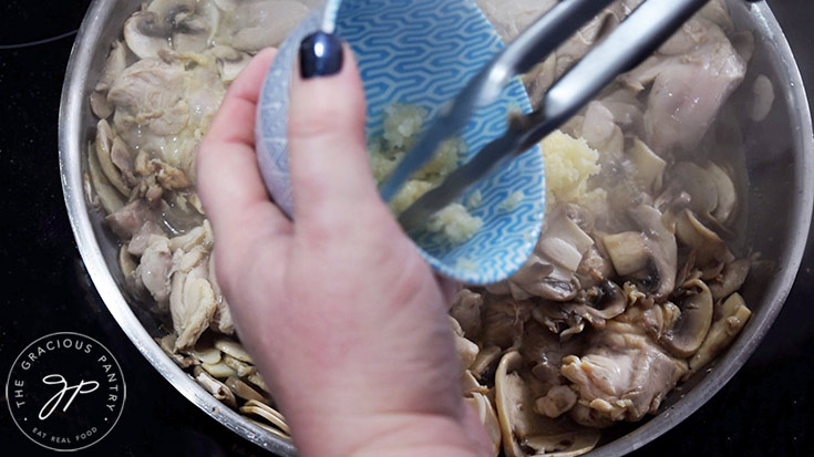 Adding pressed garlic to a skillet with chicken and mushrooms.