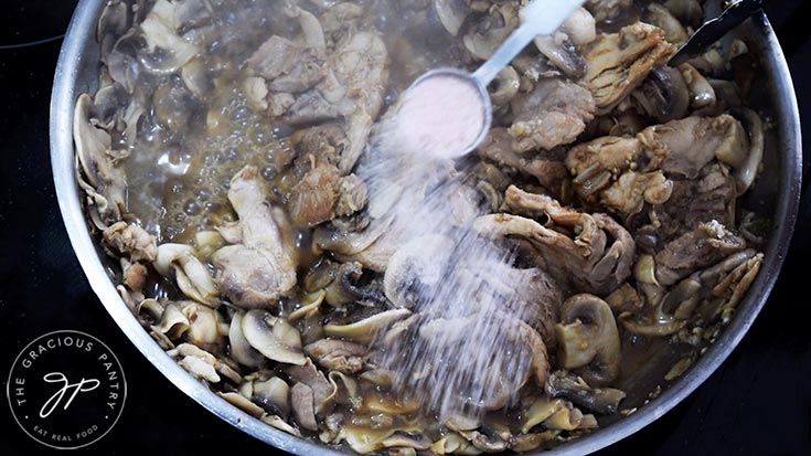 Seasoning a skillet of mushrooms and chicken with salt and pepper.