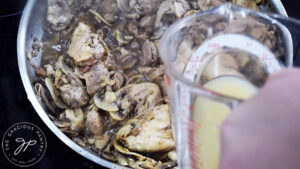 Adding chicken broth to a skillet of mushrooms and chicken.