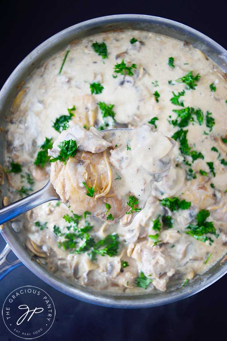 A spoon lifts some Creamy Garlic Mushroom Chicken out of a skillet.
