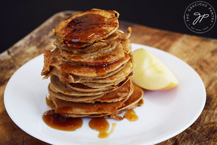 A stack of Healthy Apple Ring Pancakes with maple syrup drizzled over the top.