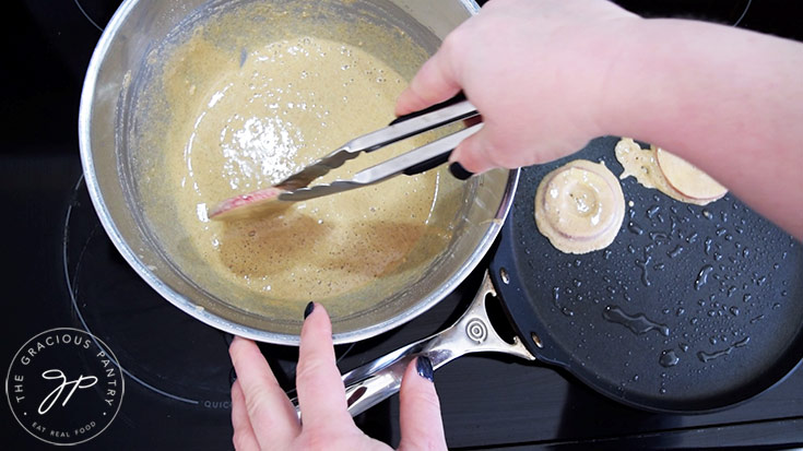 Dipping apple slices into pancake batter, then placing them on a hot skillet.
