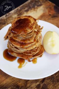 An angled overhead view of a tall stack of Healthy Apple Ring Pancakes on a white plate.